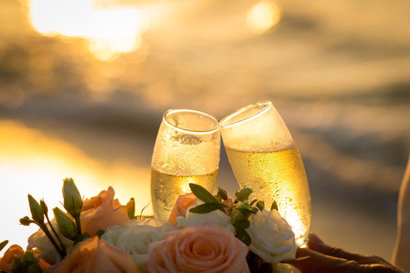 日落背景下的婚礼上的香槟酒杯和新娘花束