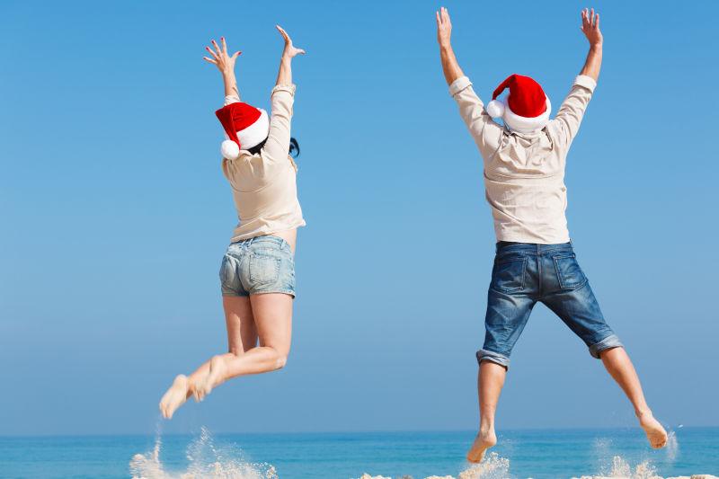带着圣诞帽子在海滩上跳跃的快乐情侣