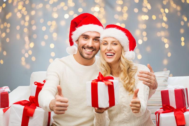 圣诞节快乐的夫妇手拿礼物在灯光背景下竖起大拇指