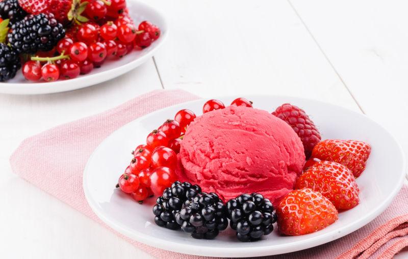 白色木桌上白色盘子里的粉红色冰淇淋和浆果
