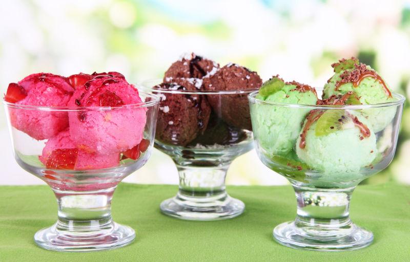 户外背景下绿色桌上的玻璃容器里的三种不同口味的冰激凌球