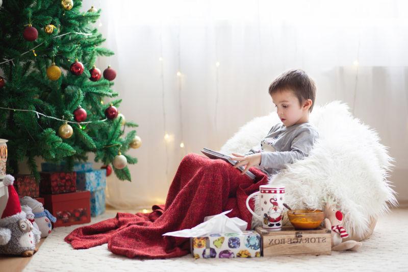 圣诞树下的小男孩坐在豆袋上玩平板
