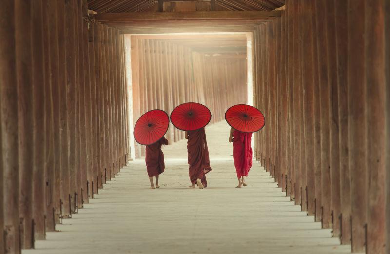 寺庙走廊里撑着红伞的三个小和尚